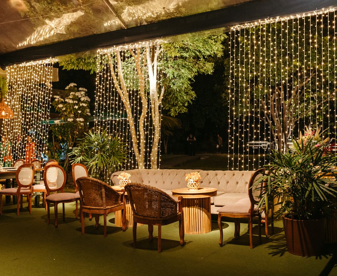 Espaço arborizado da Villa Jardim ao entardecer, com luzes douradas penduradas entre as árvores do jardim