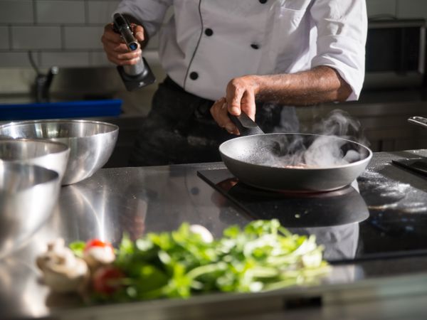 Chef italiano finalizando um prato com azeite e ervas frescas na cozinha